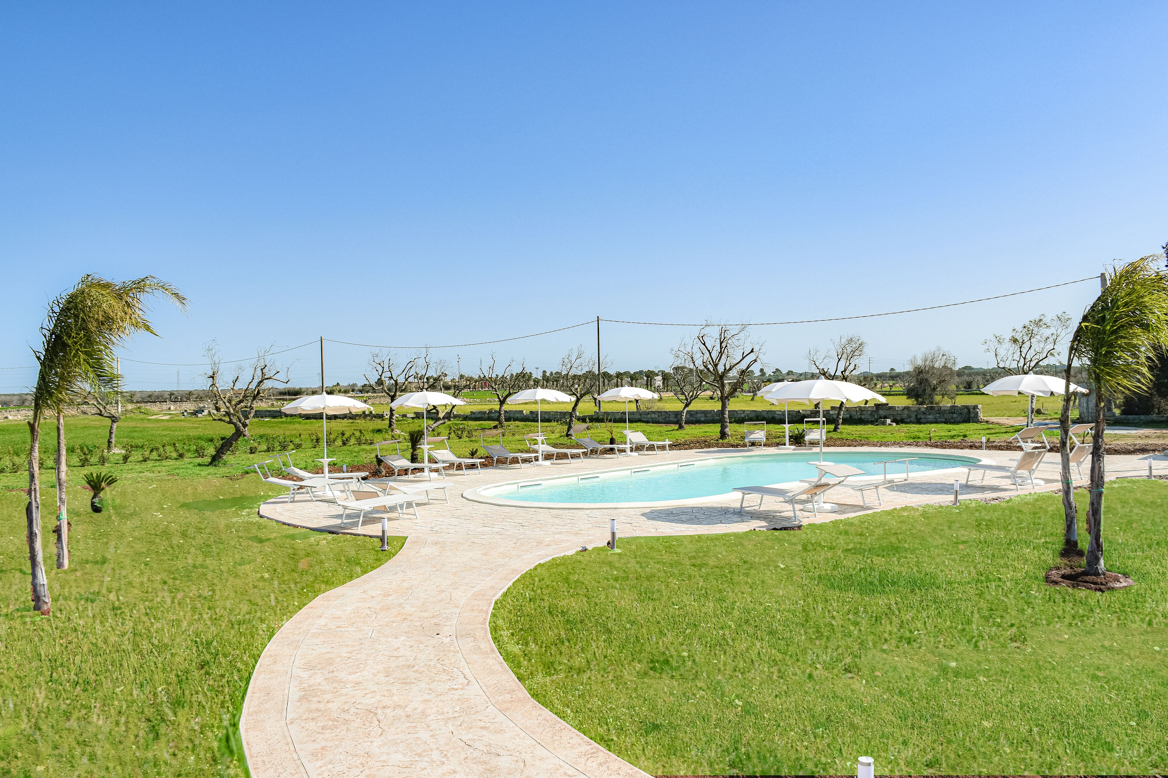 Zona de piscina amb gandules i ombrelles, envoltada d'un paisatge herbaci i arbres.