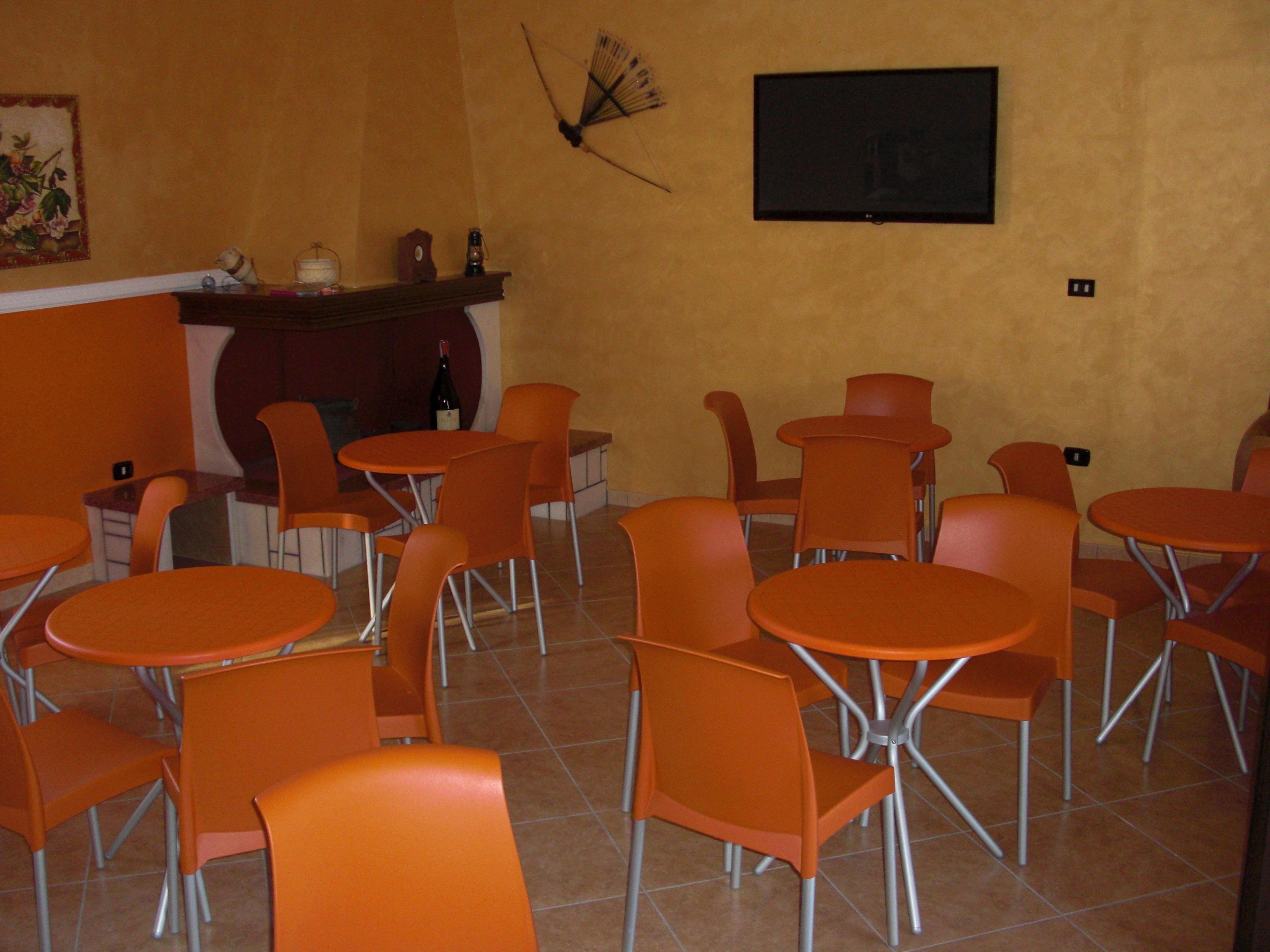 Un comedor con sillas y mesas anaranjadas, un reloj en la pared y un televisor sobre una encimera.