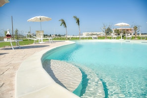 A clear swimming pool with a curved edge, surrounded by lounge chairs and umbrellas. - Il Mondo dei Sogni (Nardò)