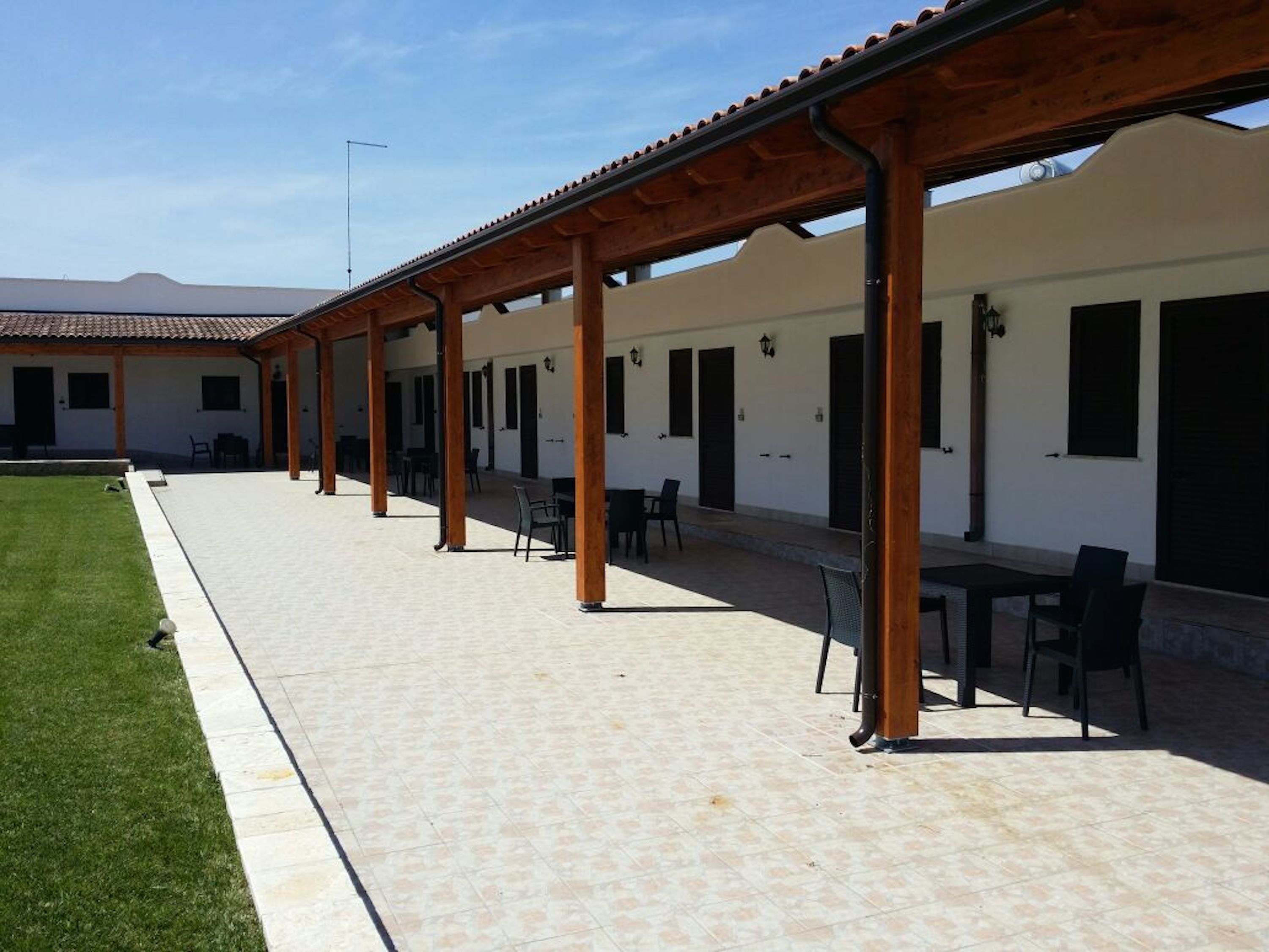 Eine überdachte Terrasse mit Tischen und Stühlen, eine Rasenfläche und ein Gebäude mit Fenstern und Türen.