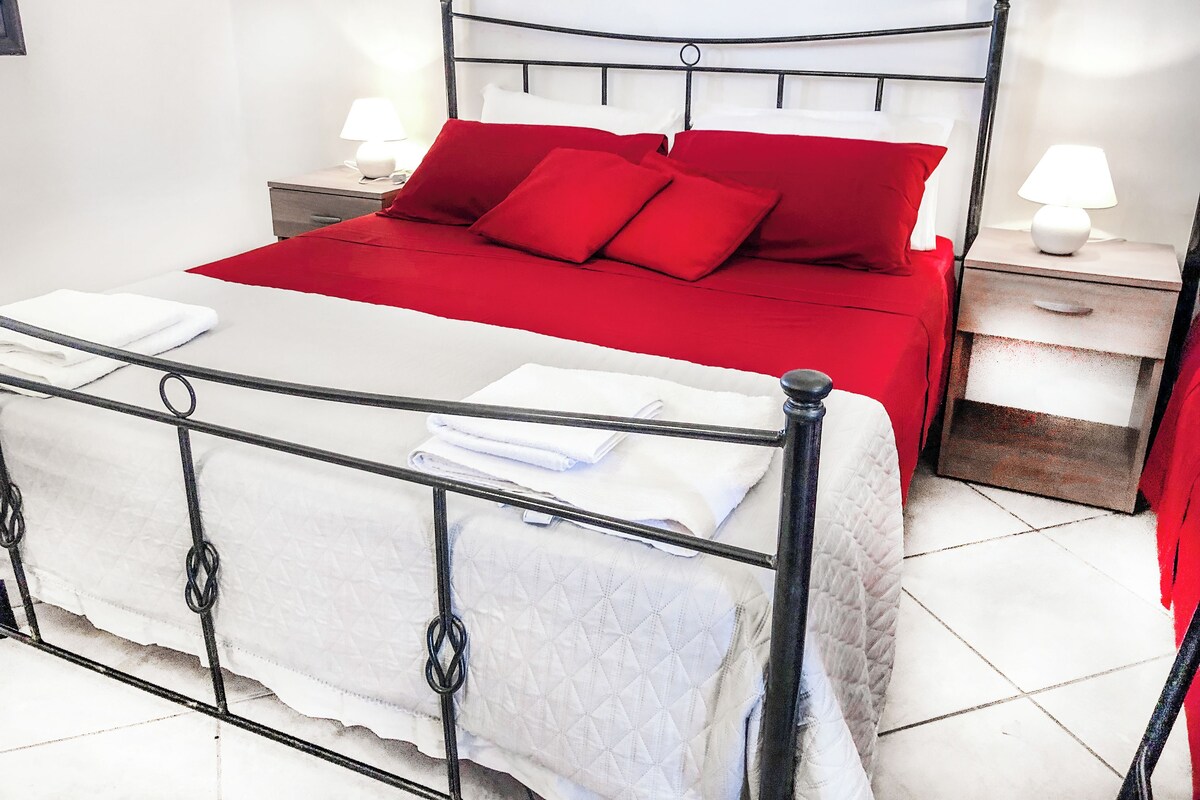 A bed with a white headboard, red bedding, and two bedside tables with lamps.
