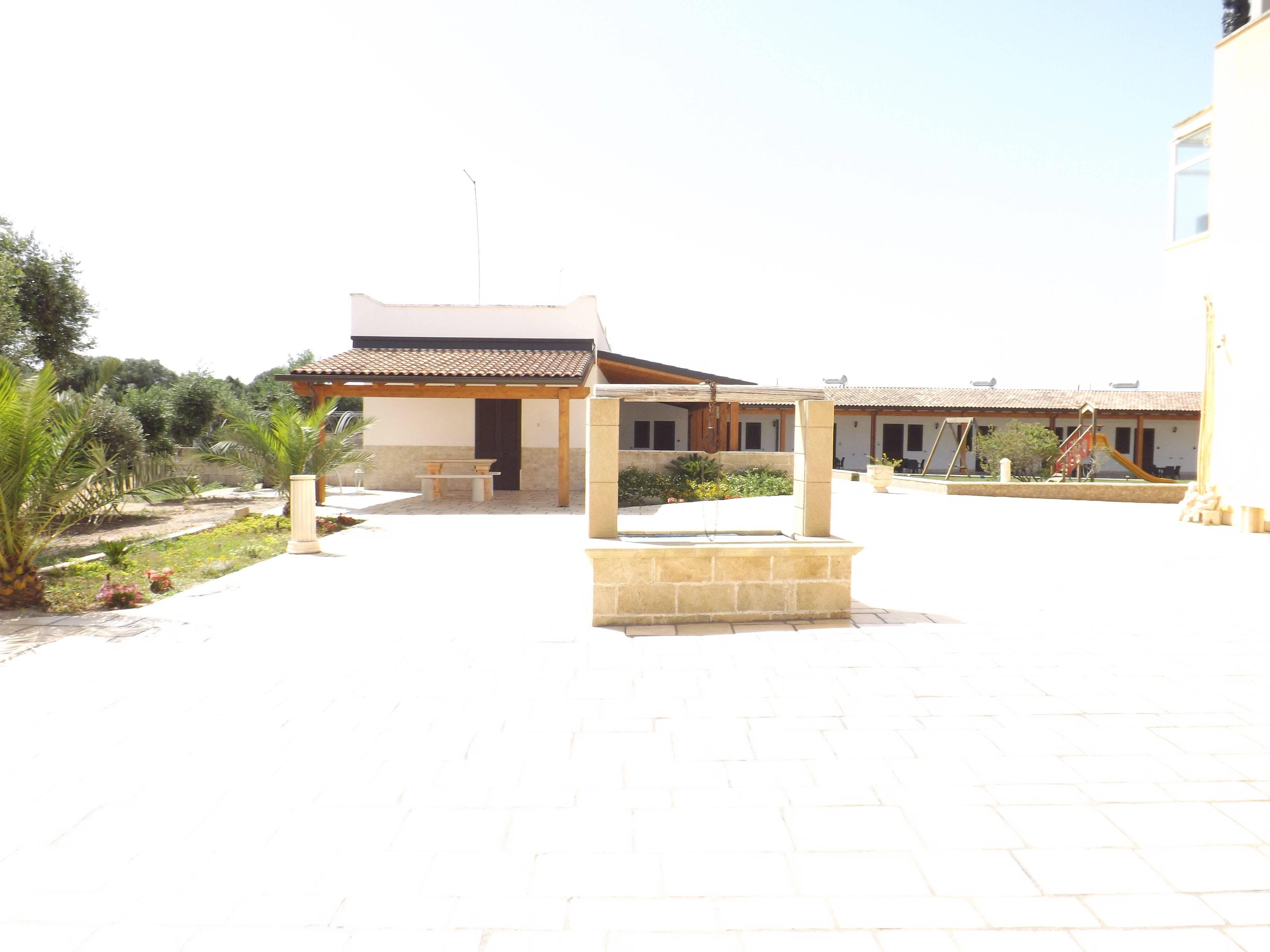 A courtyard with a covered seating area, a children's play area, and a building with a tiled roof.