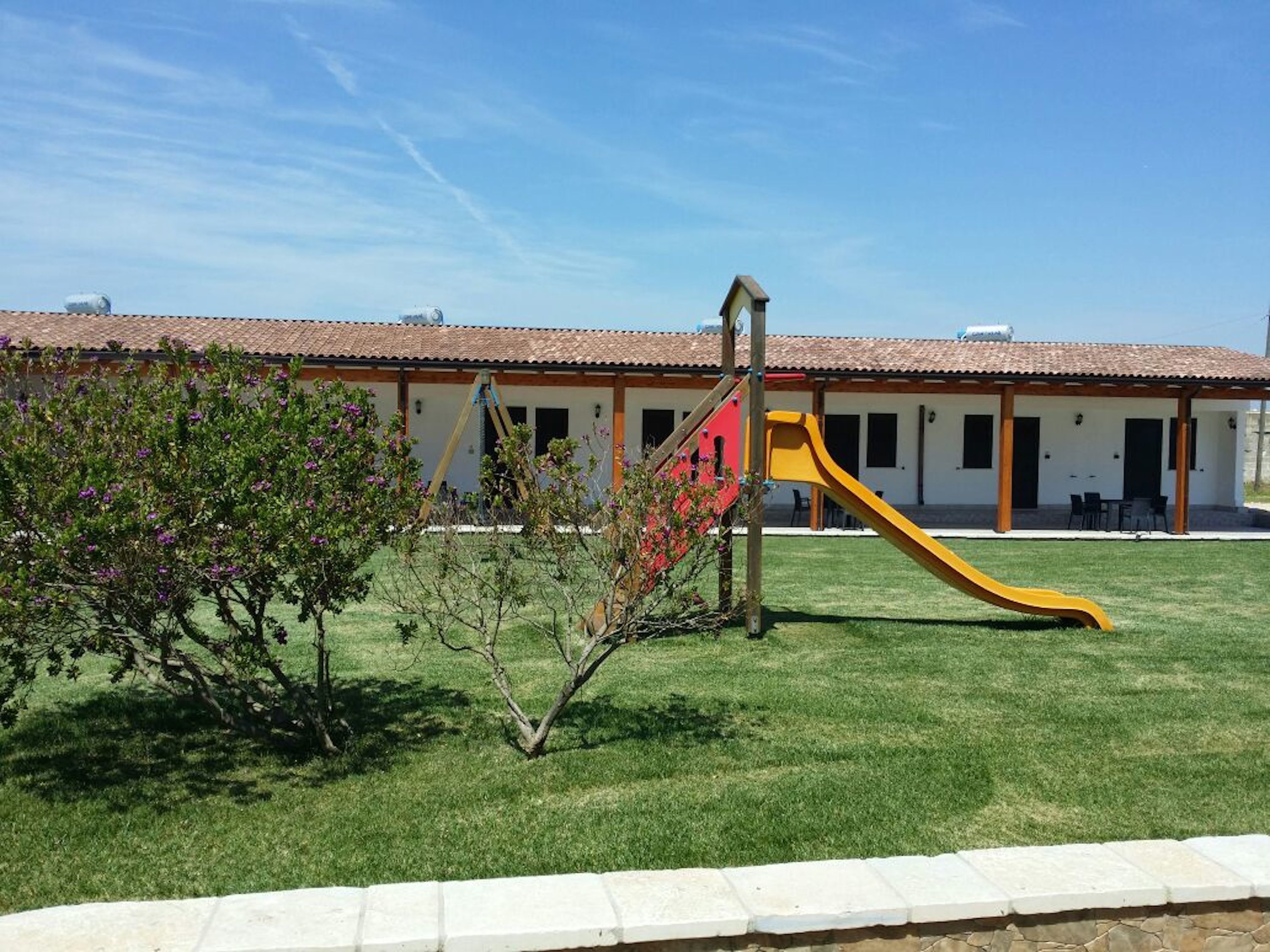 A building with a red and yellow slide, a covered patio, and a lawn.