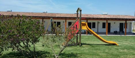 A building with a red and yellow slide, a covered patio, and a lawn.