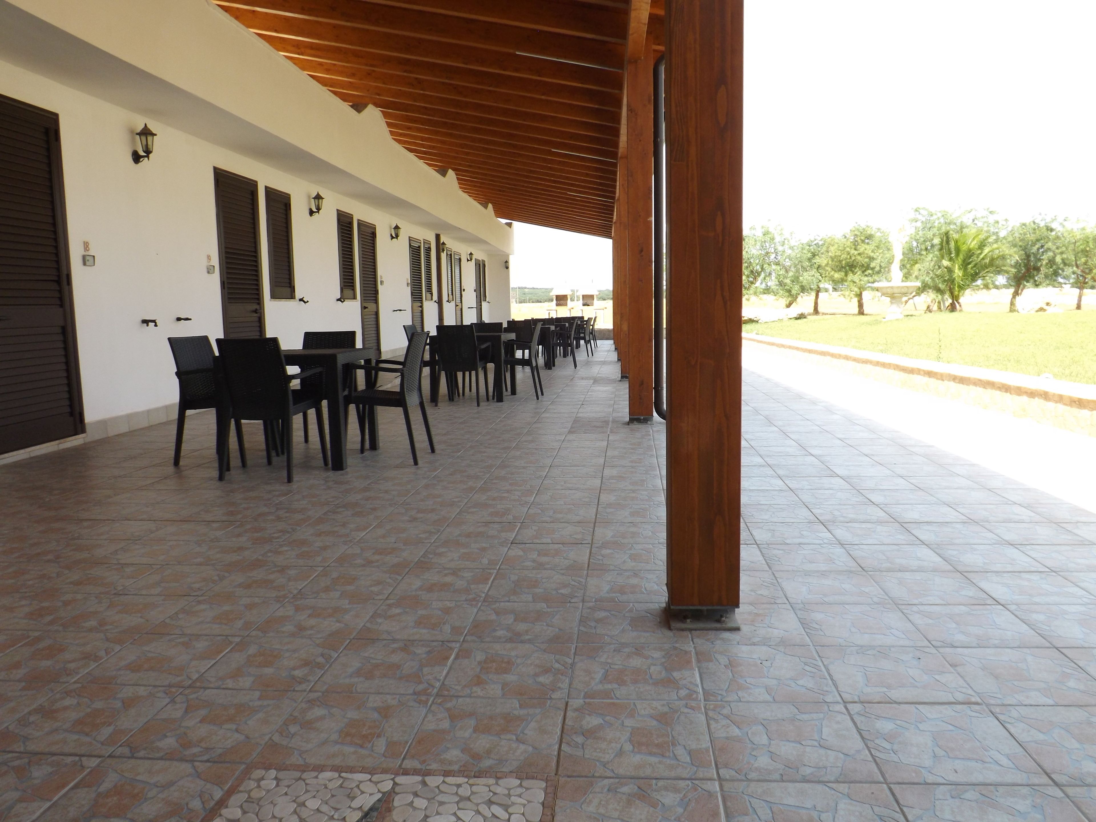 Une terrasse extérieure couverte, dotée d’un sol carrelé et de chaises noires disposées en rangées.