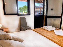 A hotel room with a bed, a chair, a window with blinds, and a view of the outdoors.