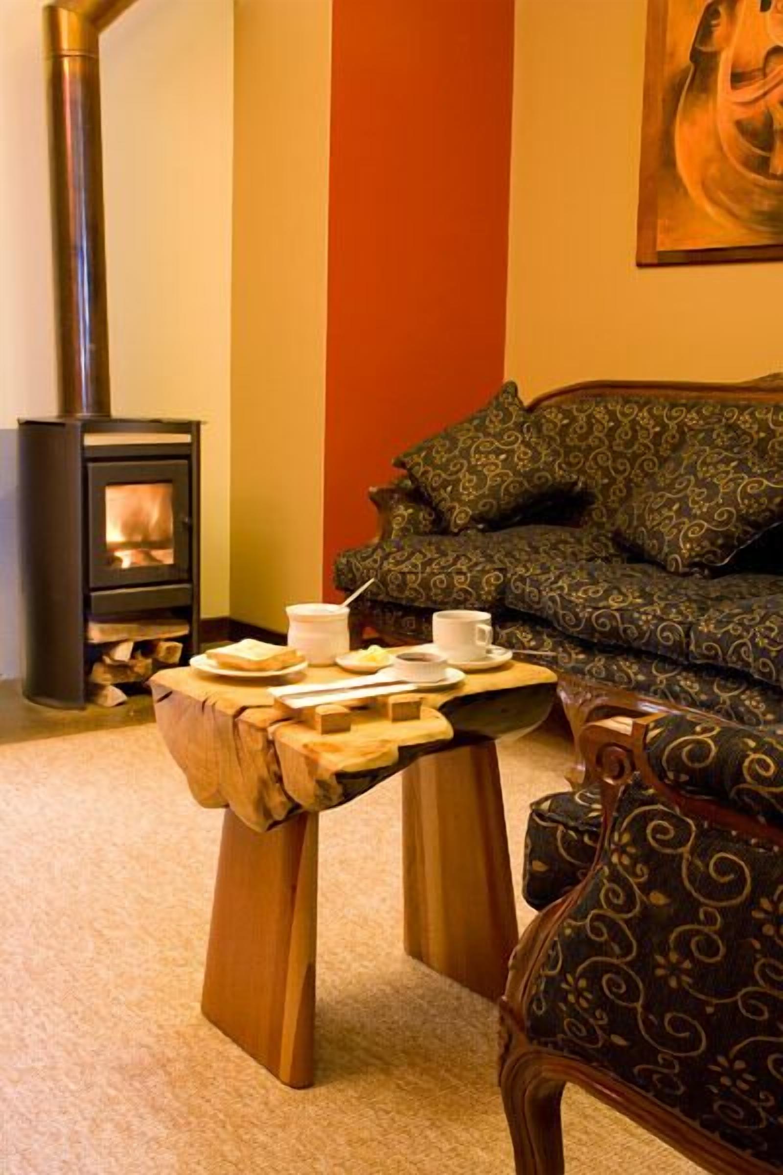 A cozy living room with a wood-burning stove, a sofa with patterned cushions, and a small wooden table with a cup and plate.