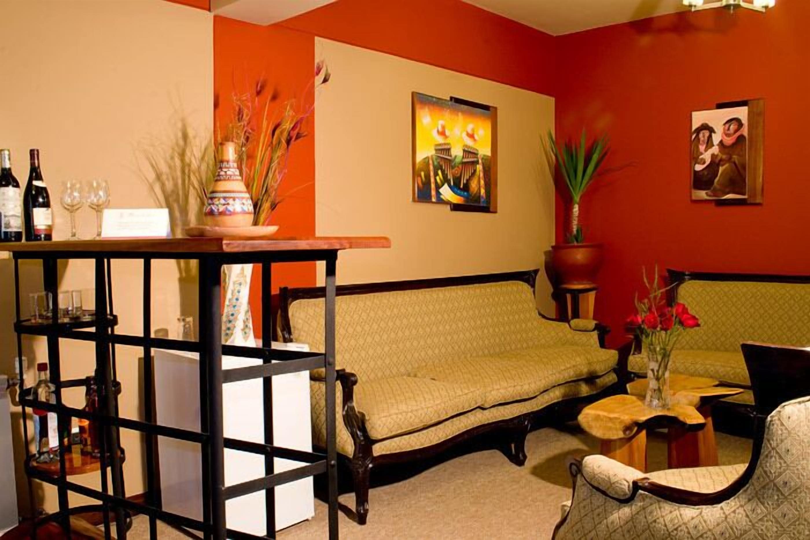 A room with a sofa, a small table with a vase of flowers, and a shelf with bottles and glasses.