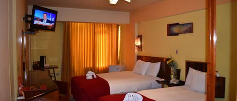 A hotel room with two beds, a TV mounted on the wall, a desk with a chair, and a window with curtains.