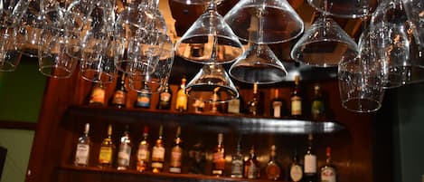 A bar area with multiple hanging wine glasses and a shelf of various liquor bottles.