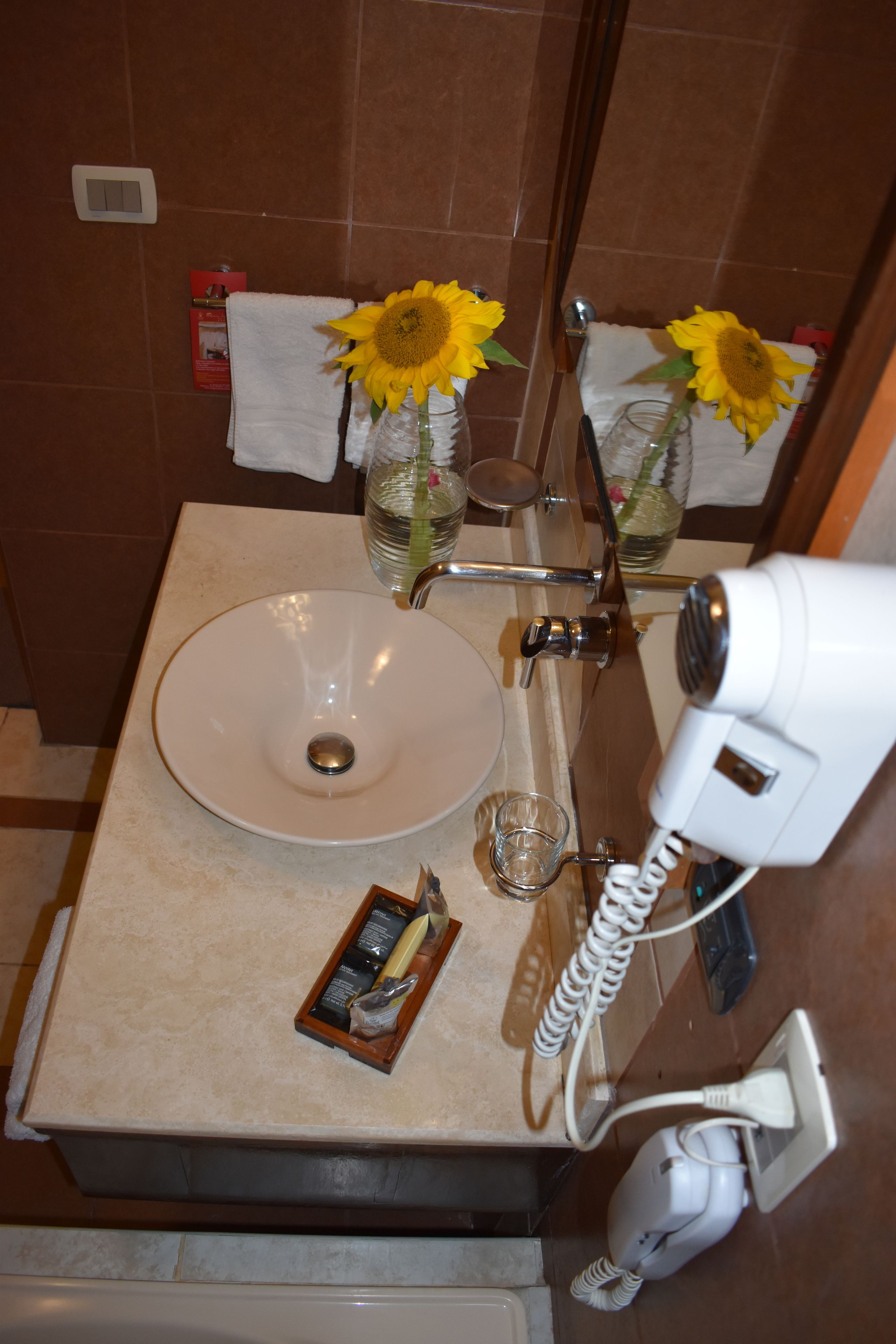 A bathroom with a sink, a hairdryer, and two vases with sunflowers.