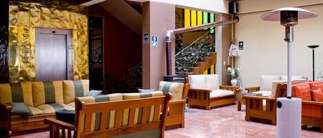 A spacious lobby with a marble floor, wooden furniture, a staircase, and a stone wall.