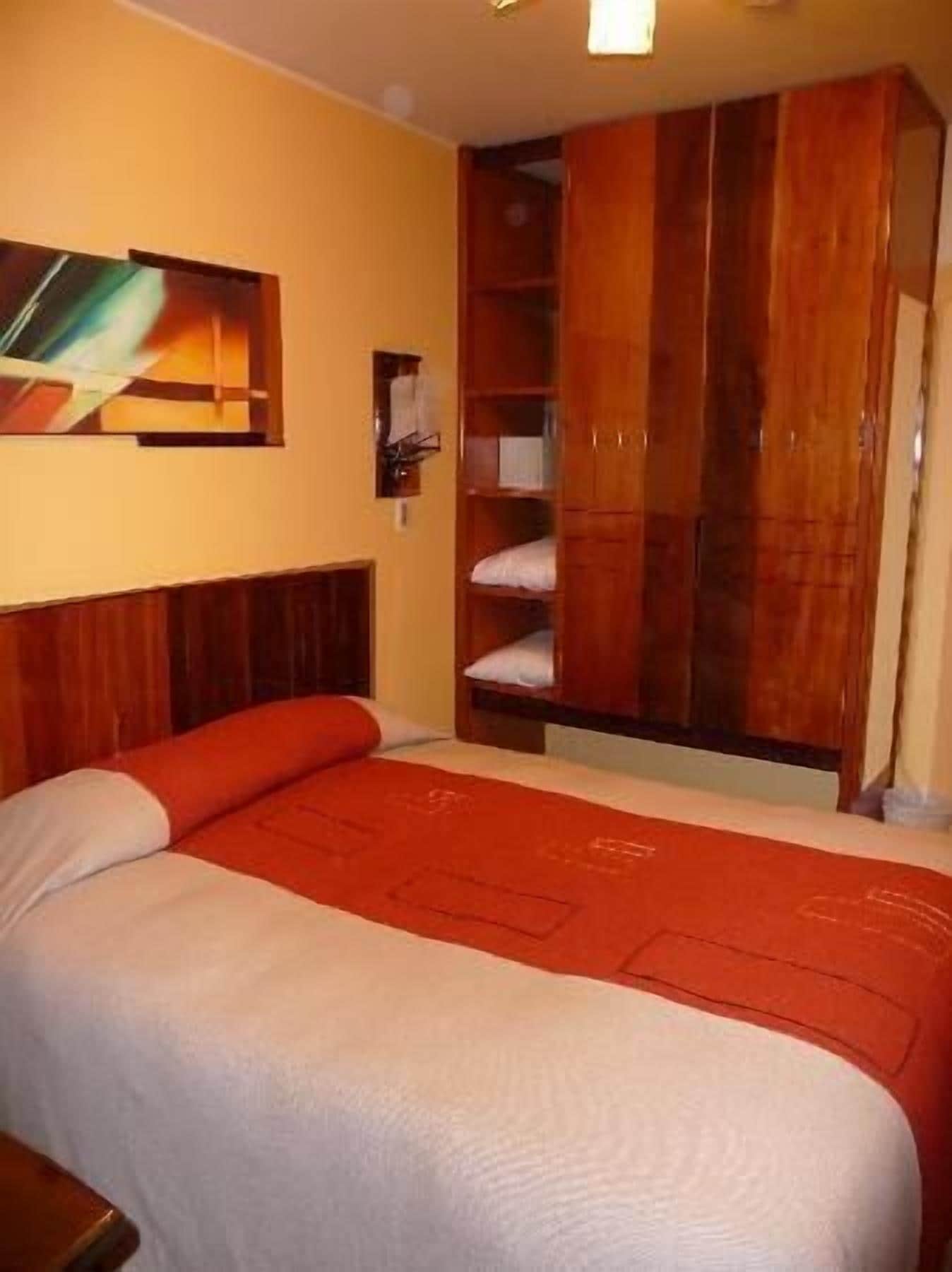 A hotel room with a bed, a wooden wardrobe, and a painting on the wall.