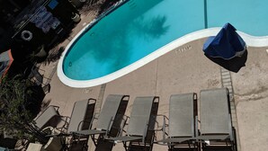 En swimmingpool med solstolar och parasoller, omgiven av en betongplattform.
