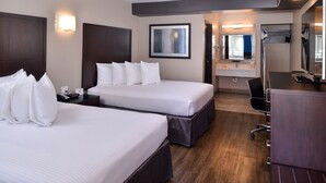 Ett hotellrum med två sängar, ett skrivbord, en stol, en spegel och ett badrum som syns genom en öppen dörr.