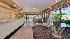 A hotel lobby with a marble floor, a reception desk, a seating area with a glass table, and a view of the outdoors. - Tarzana Inn (Tarzana)