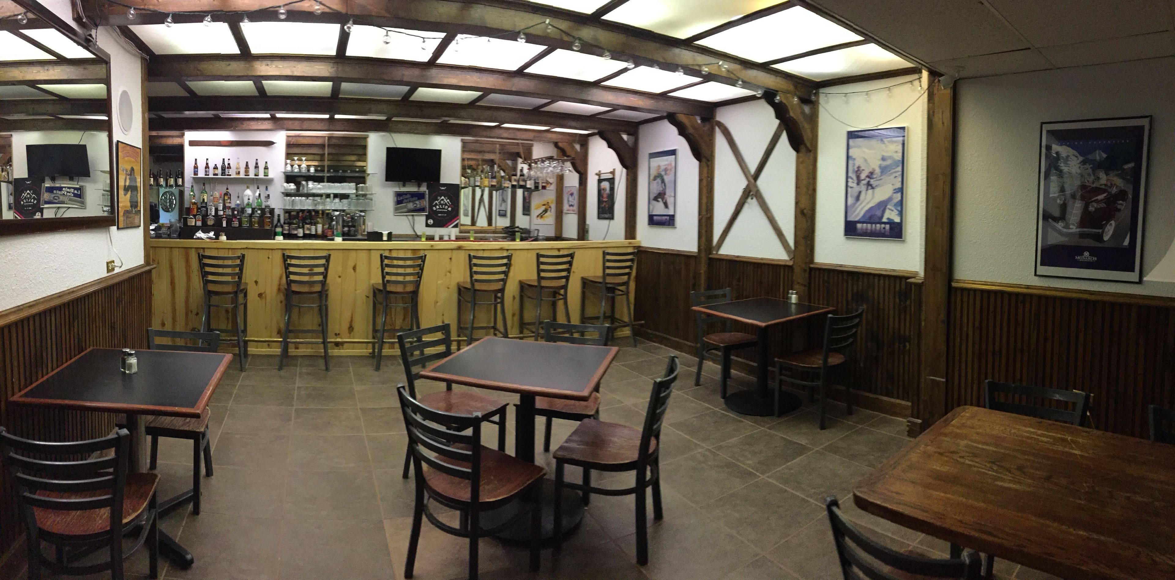 A restaurant with wooden tables and chairs, a bar area with bottles and glasses, and posters on the walls.
