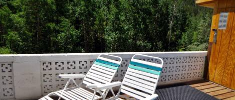 A deck with two lounge chairs and a small table, overlooking a forested mountain.