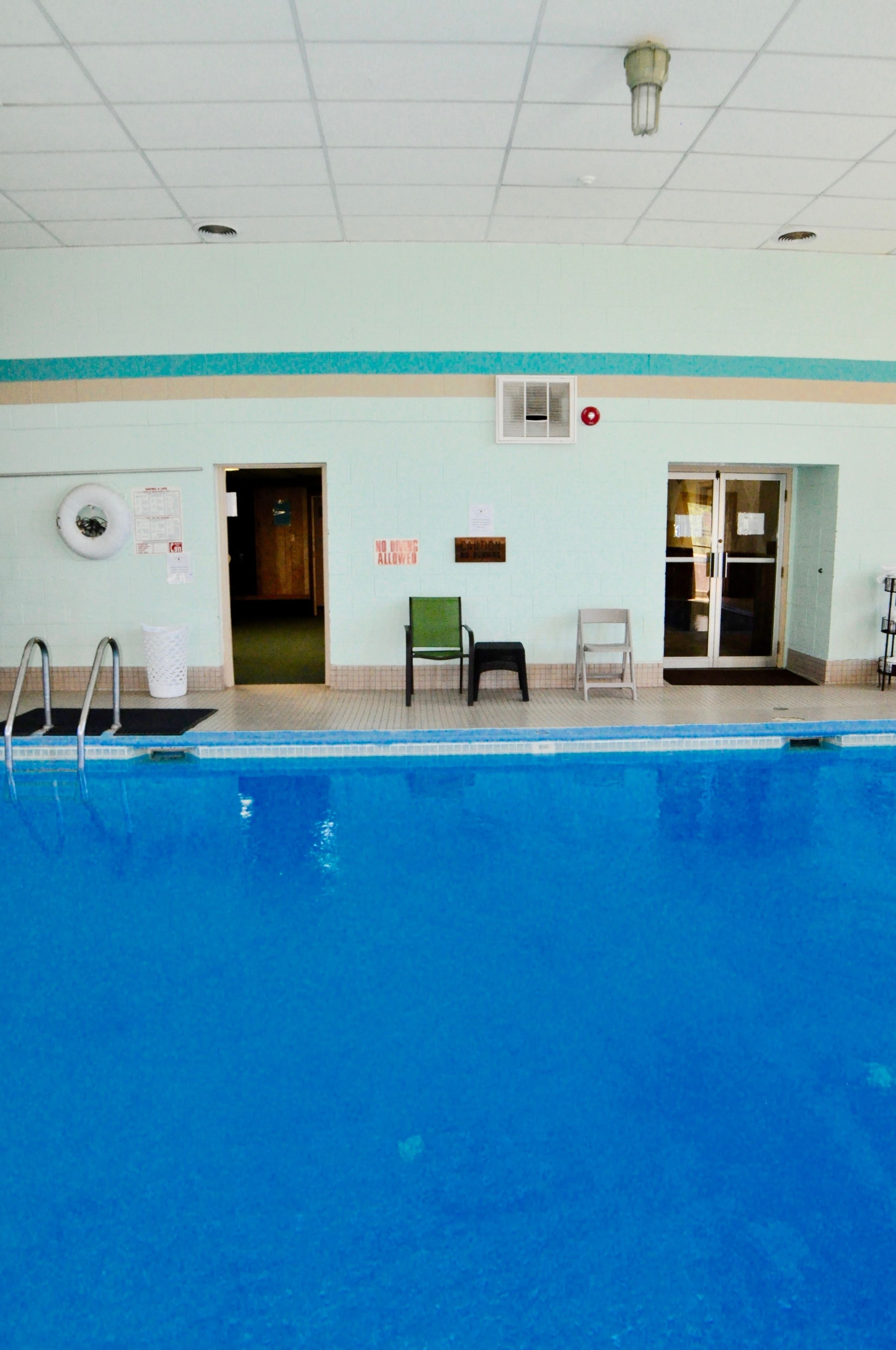An indoor swimming pool with a tiled floor, a green chair, a white chair, and a door leading to another room.