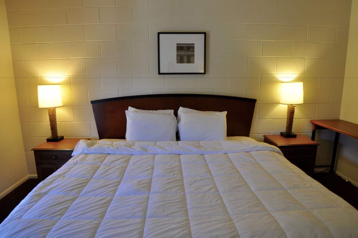 A neatly made bed with white bedding, two bedside lamps, and a framed picture on the wall above the bed.
