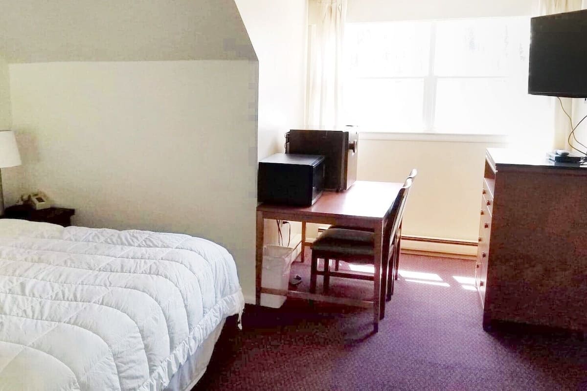 A hotel room with a bed, a desk, a chair, a television, and a window.