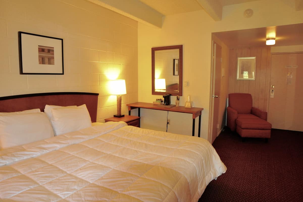 A hotel room with a bed, a desk, a chair, and a door.