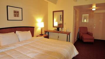 Quarto de hotel com cama, escrivaninha, cadeira e porta.