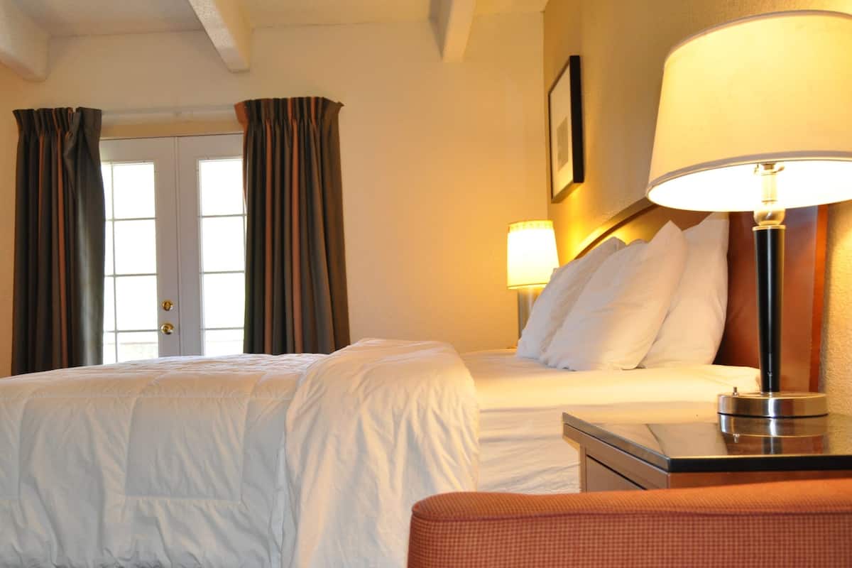 A hotel room with a bed, a chair, a desk, and a lamp. There are curtains on the windows.