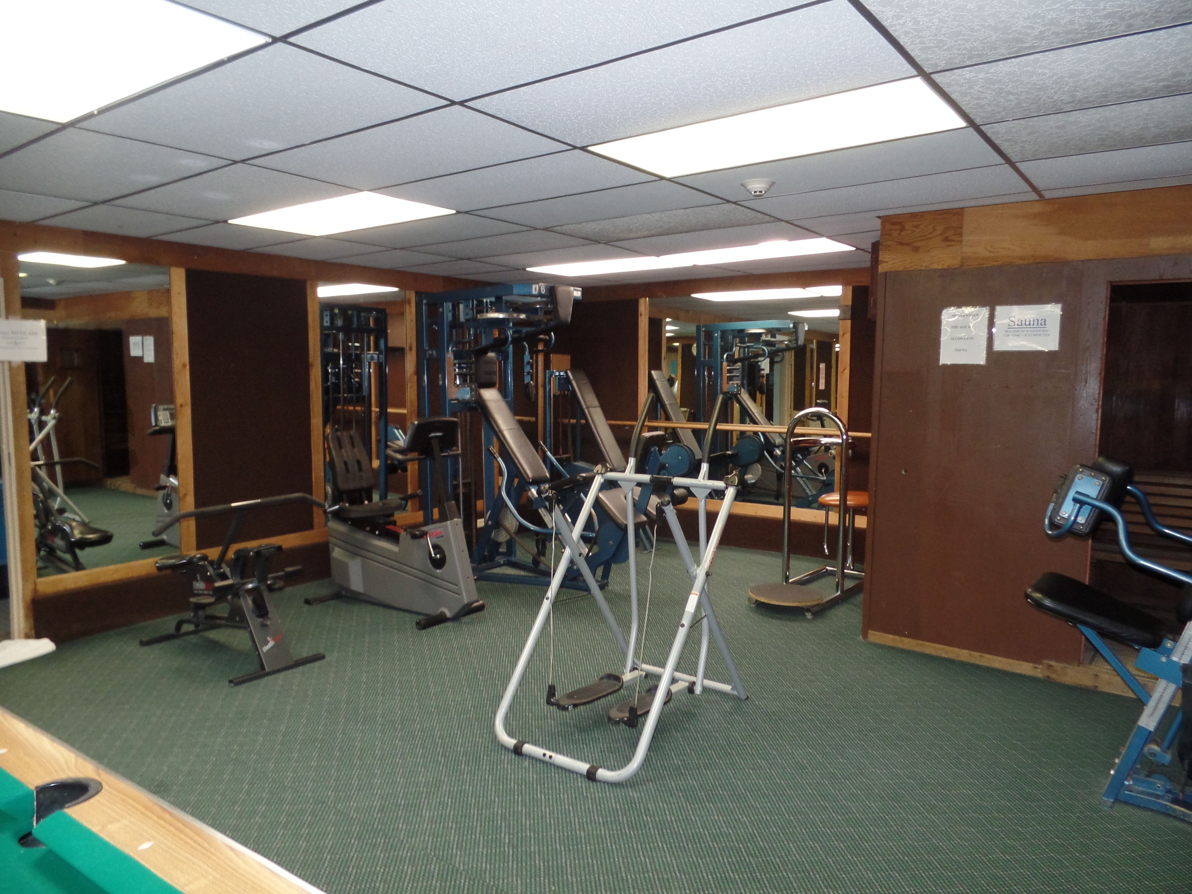 A gym with various exercise equipment, mirrors, and a sauna sign.
