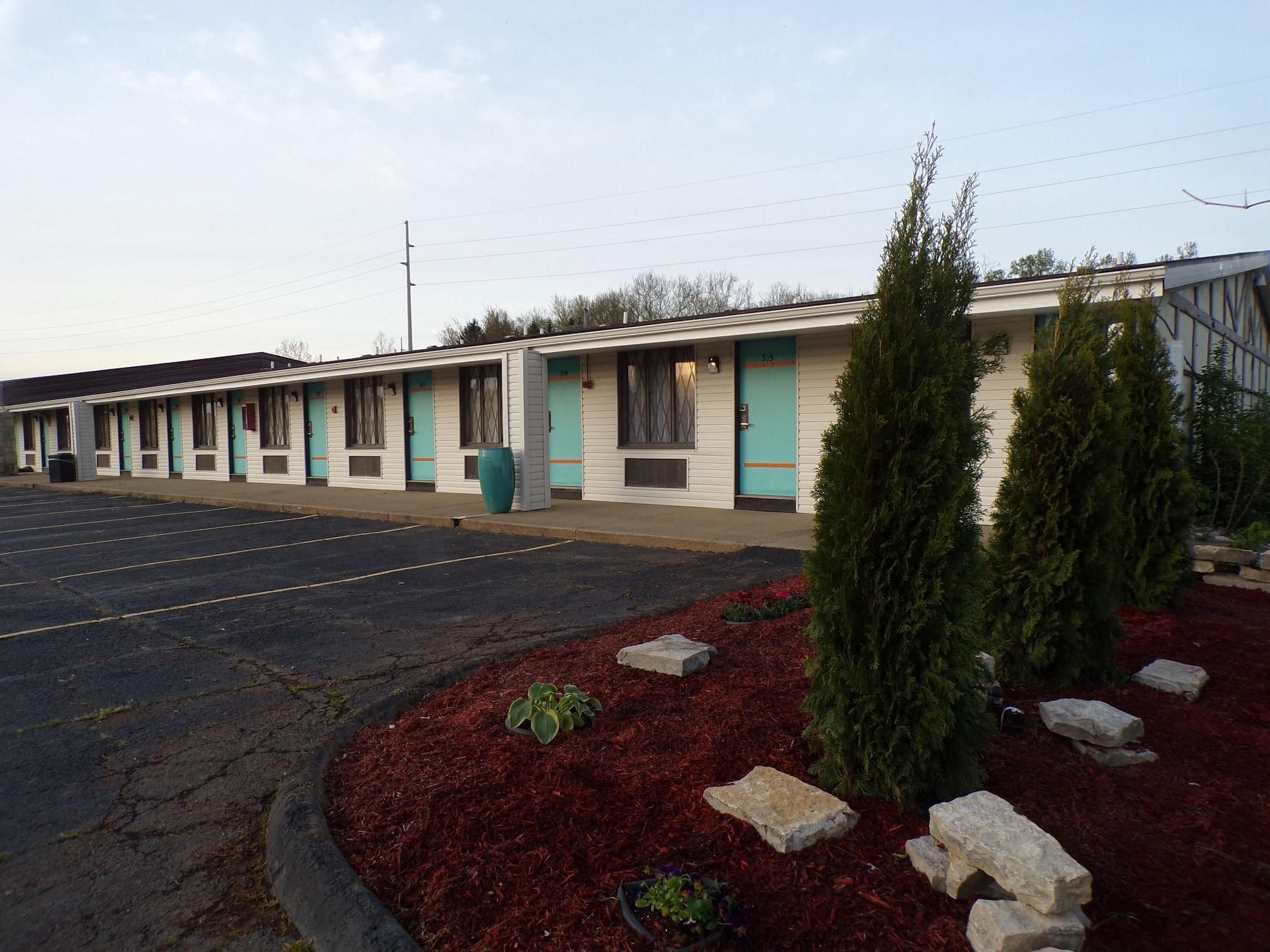 A motel with a row of rooms, a parking lot, and a landscaped area with plants and rocks.