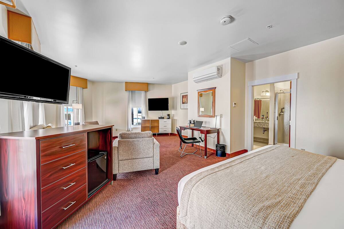Ein Hotelzimmer mit Bett, Schreibtisch, Stuhl, Fernseher, Kleiderschrank und einem durchgegangene Tür sichtbaren Badezimmer.