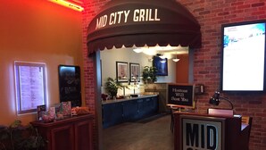 De ingang van Mid City Grill, met een bord waarop staat dat een gastvrouw je een tafel geeft.