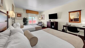 Hotelkamer met twee bedden, een bureau, een stoel, een televisie en een groot raam.