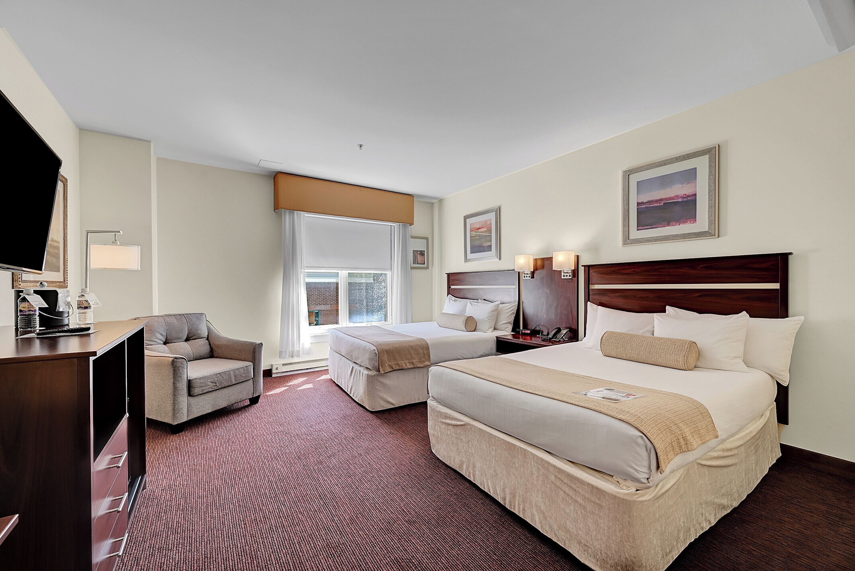 A hotel room with a large bed, a smaller bed, a desk, a chair, and a television.