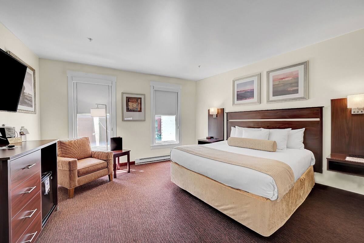 Ein Hotelzimmer mit einem großen Bett, einem Schreibtisch, einem Stuhl und zwei Fenstern.