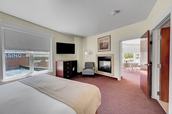 A hotel room with a large bed, a flat-screen TV, a fireplace, and a view of a casino through the window.