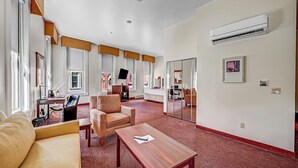 Ruime hotelkamer met een groot raam, een flatscreen televisie, een bank, een stoel, een kleine tafel en een roodgekleurd tapijt.