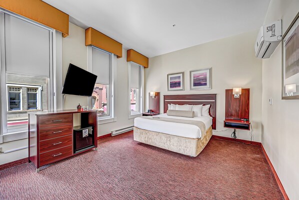 A hotel room with a bed, a TV, a dresser, and a window.