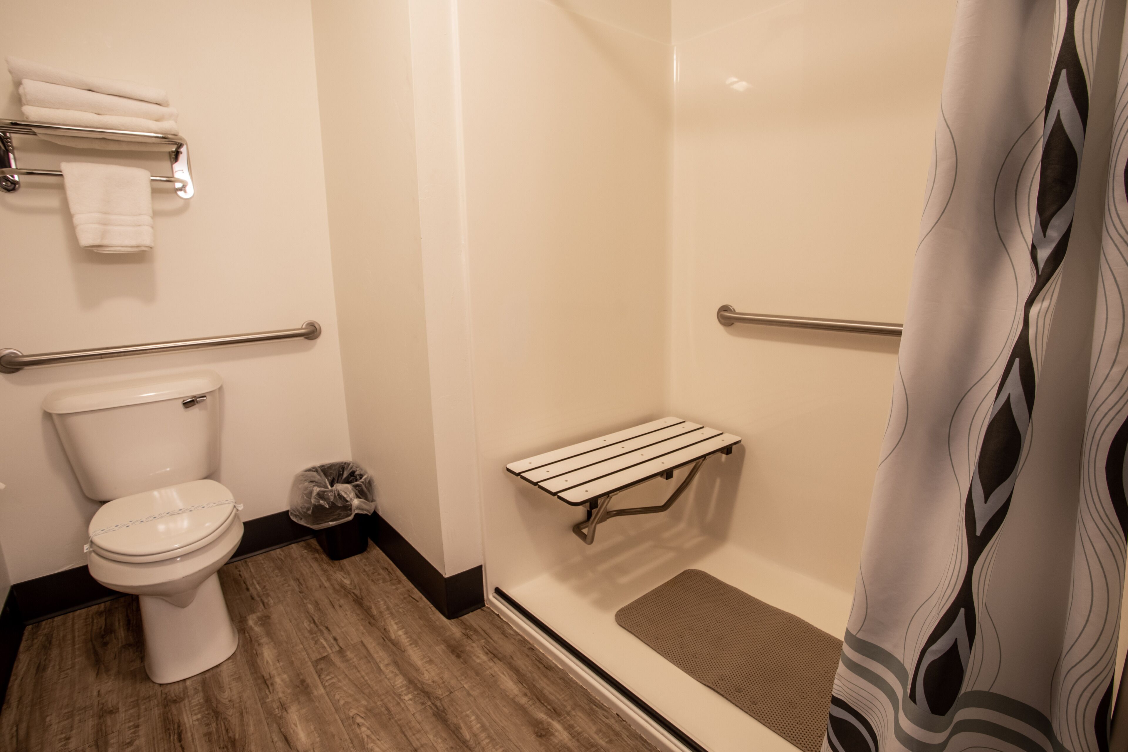 Ein Badezimmer mit Toilette, Handtuchhalter, einer Haltestange, einer Duschkabine und einem waschbärigem Duschvorhang.