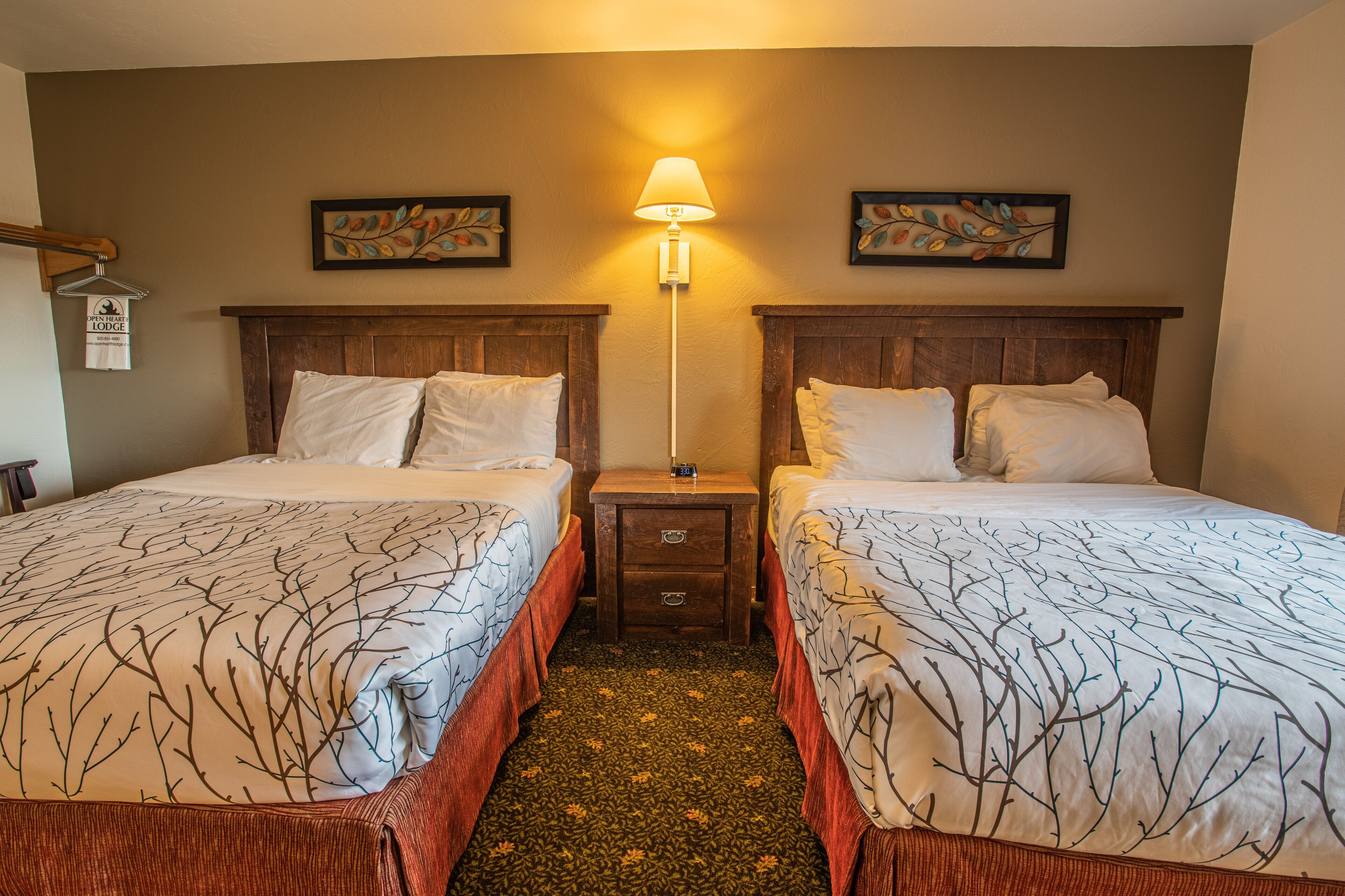 A hotel room with two beds, a nightstand, a lamp, and artwork on the walls.