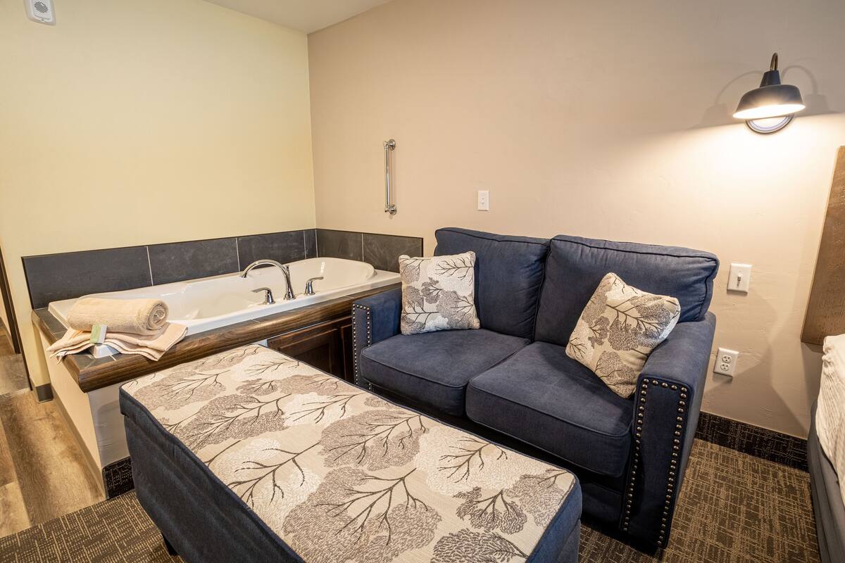 A bathroom with a bathtub, a blue sofa, and a patterned ottoman.