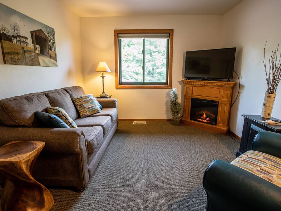 A living room with a sofa, a wooden coffee table, a television, a fireplace, and a window.