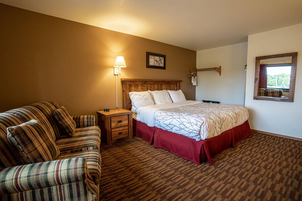 A hotel room with a bed, a wooden nightstand, a lamp, a couch, and a window with a view.