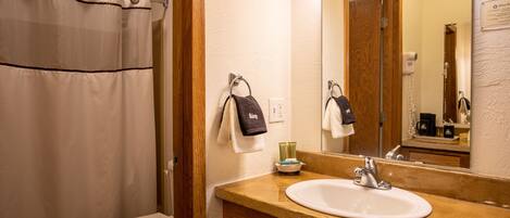 A bathroom with a shower curtain, a toilet, a sink with a mirror, and a towel rack with towels.