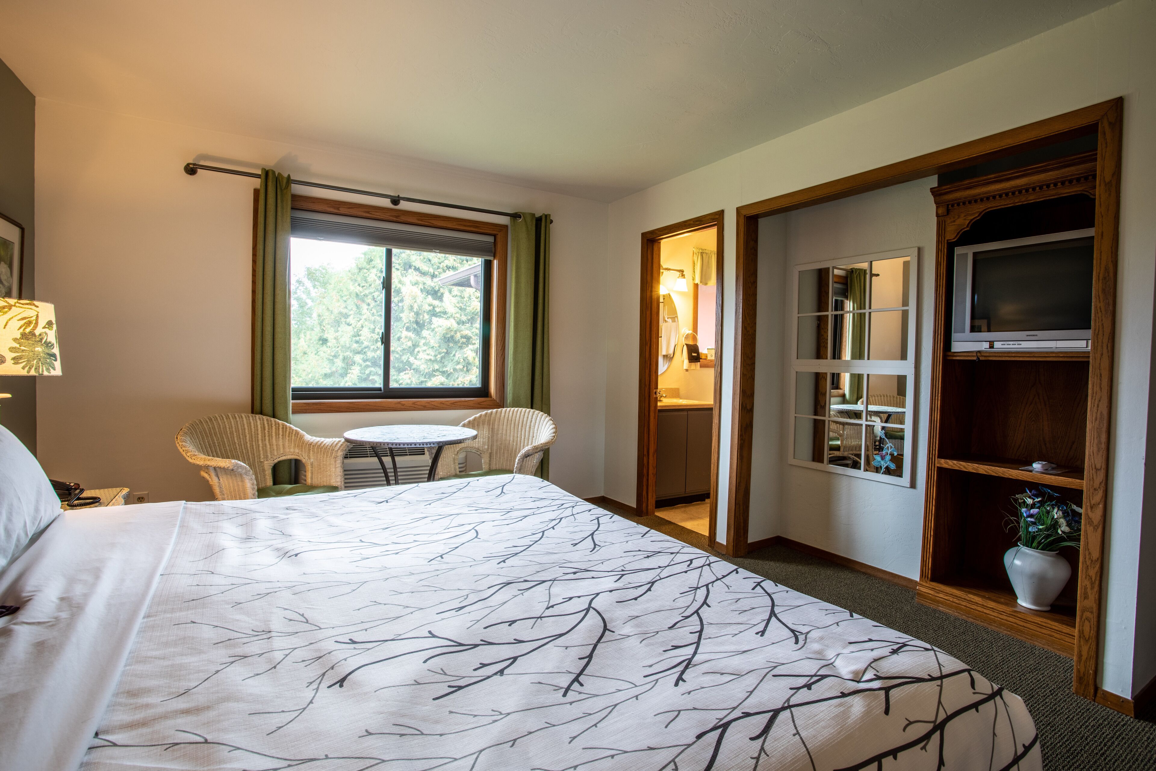 A hotel room with a large bed, a small round table, two chairs, a TV, and a wooden cabinet.