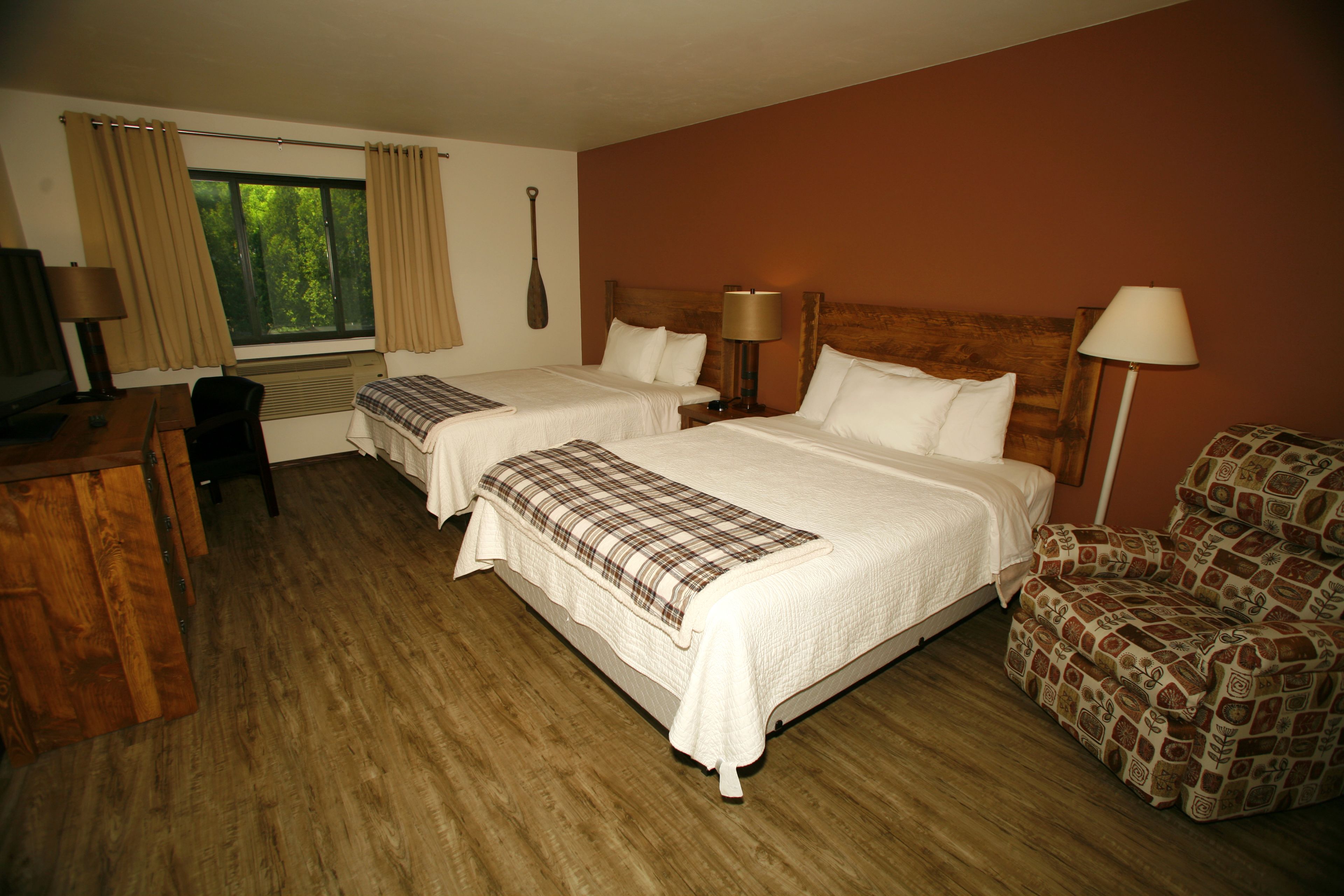 Habitación de hotel con dos camas, un escritorio, una silla y un ventanal con cortinas.
