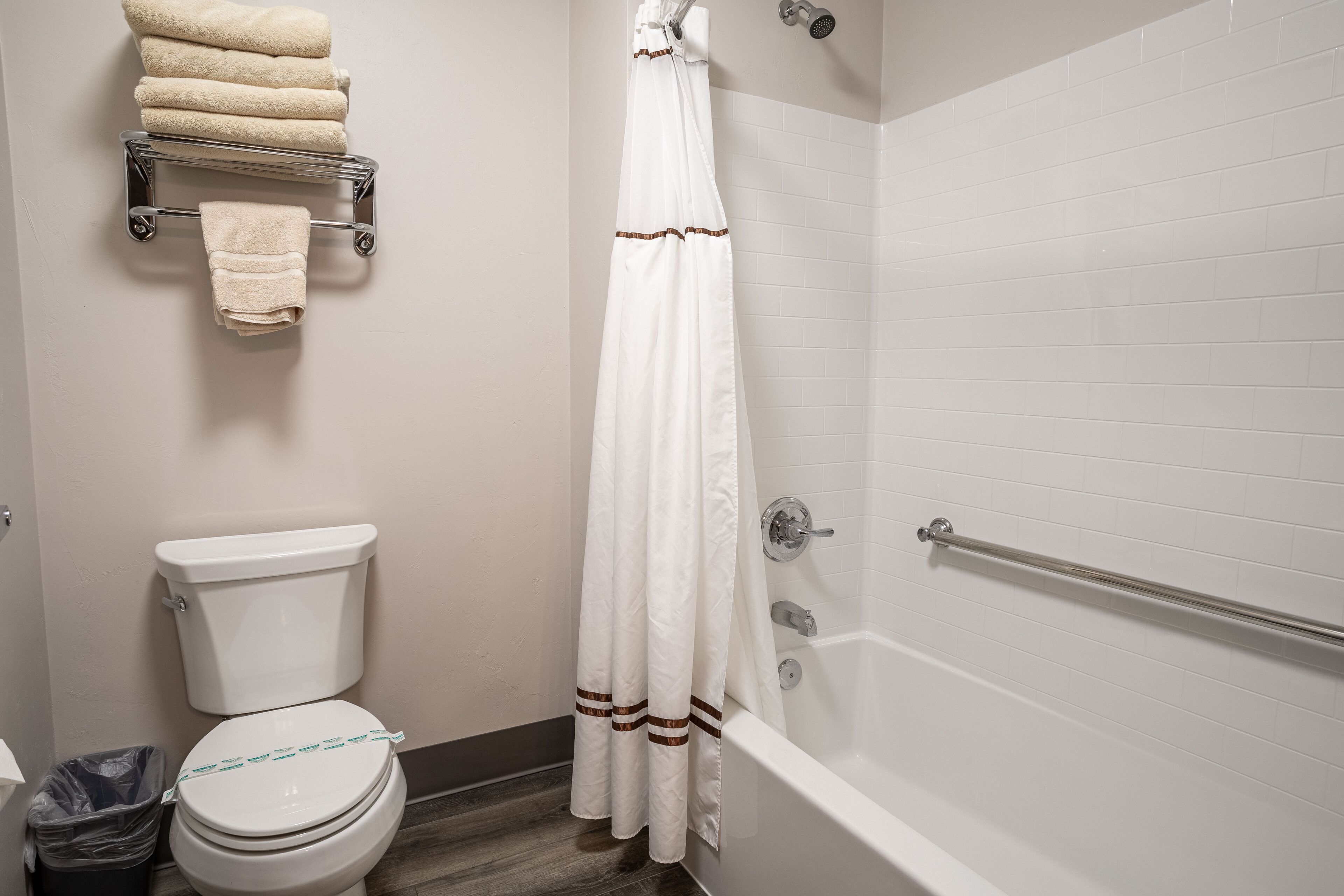 A bathroom with a toilet, a shower with a glass door, and a towel rack with folded towels.