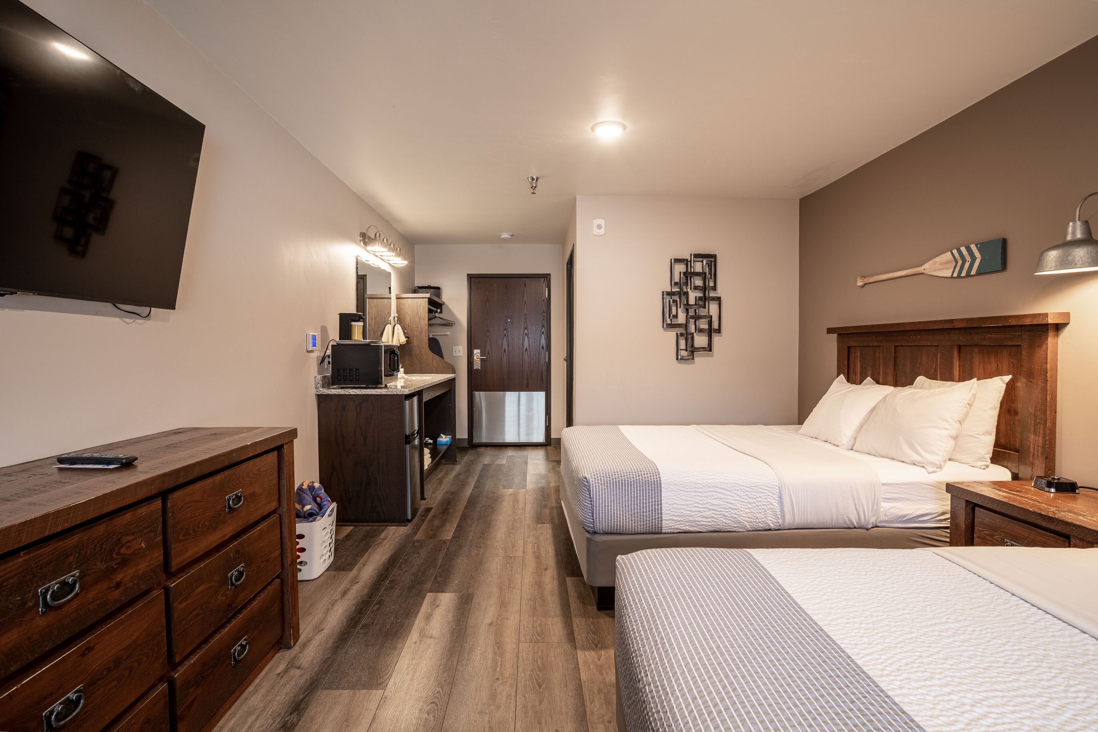 A hotel room with a large bed, a smaller bed, a desk, a dresser, a TV, and a bathroom visible through an open door.