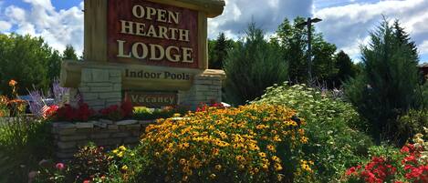 A sign for Open Hearth Lodge with a stone base, indoor pools, and a vacancy notice.