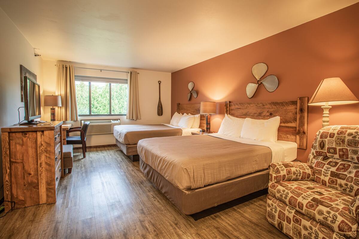 A hotel room with two beds, a desk, a chair, and a window with curtains.